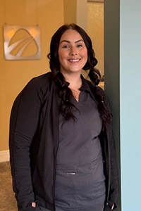 Dental office staff member in gray scrubs smiling in modern reception area with logo signage