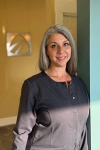 Dental team member Stephanie in black uniform leaning by teal wall in office lobby with logo sign.